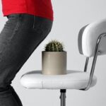 Người phụ nữ đứng không dám ngồi xuống ghế có đặt cây xương rồng, mô phỏng cảm giác đau đớn dữ dội khi bị bệnh trĩ nặng.